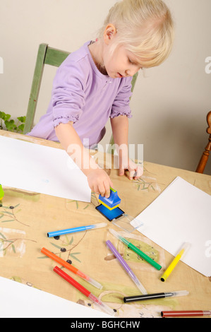 Stock photo d'une fillette de quatre ans à l'aide de timbres d'encre lors d'une session de jeu créatif. Banque D'Images