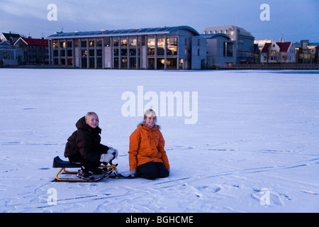 Deux filles avec un traîneau neige sur un lac gelé (Tjornin). Le centre-ville de Reykjavik, Islande.