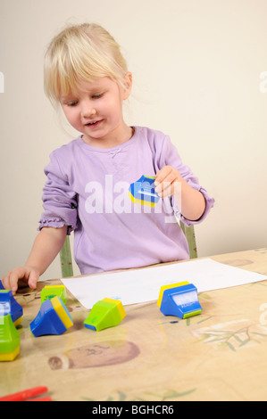 Stock photo d'une fillette de quatre ans à l'aide de timbres d'encre lors d'une session de jeu créatif. Banque D'Images