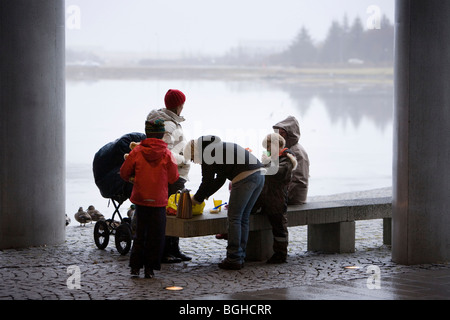 Une famille bénéficiant d'un pique-nique à l'extérieur pendant un jour pluvieux et brumeux. Hôtel de ville de Reykjavik, le centre-ville de Reykjavik, Islande. Banque D'Images