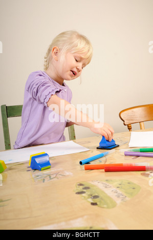 Stock photo d'une fillette de quatre ans à l'aide de timbres d'encre lors d'une session de jeu créatif. Banque D'Images