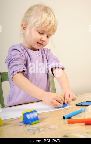 Stock photo d'une fillette de quatre ans à l'aide de timbres d'encre lors d'une session de jeu créatif. Banque D'Images