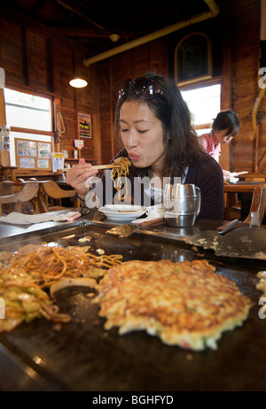 Okonomi yaki. De style japonais, des crêpes salées. Japanese woman eating noodles Japon Banque D'Images
