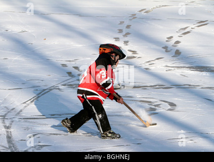 Un jeune garçon habillé en équipement de hockey Devils de New York sur la glace avec son casque mais pas de rondelle stick Patins. Banque D'Images