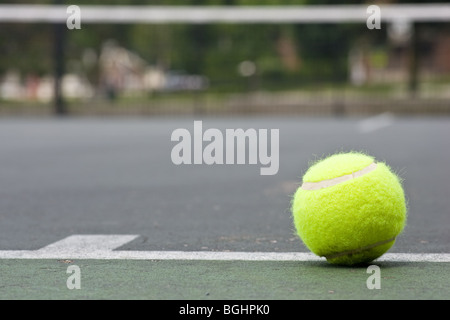 Un gros plan d'une balle de tennis jaune juste à l'extérieur de la ligne de base de l'asphalte sur un court de tennis, avec un flou en arrière-plan net Banque D'Images