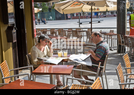 Couple d'âge moyen assis café à l'extérieur de lire les journaux Banque D'Images