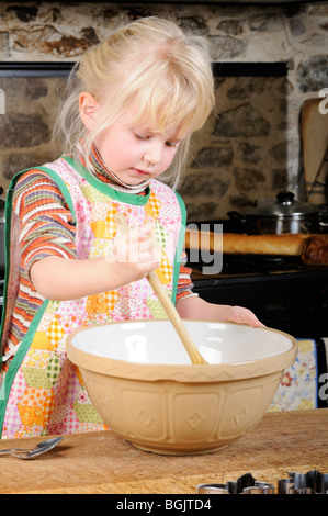 Stock photo d'une fillette de quatre ans à l'aide d'une cuillère en bois pour mélanger un peu la pâte pour faire des biscuits. Banque D'Images