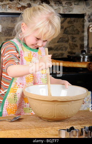 Stock photo d'une fillette de quatre ans à l'aide d'une cuillère en bois pour mélanger un peu la pâte pour faire des biscuits. Banque D'Images