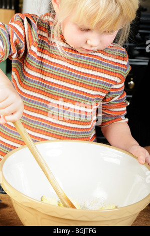 Stock photo d'une fillette de quatre ans à l'aide d'une cuillère en bois pour mélanger un peu la pâte pour faire des biscuits. Banque D'Images