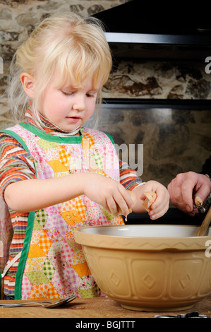 Stock photo d'une fillette de quatre ans, la fissuration des oeufs dans un bol à mélanger, prêts à faire des cookies. Banque D'Images