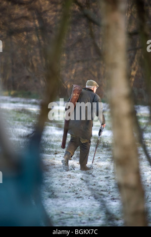 Homme avec un fusil de chasse à l'arme et tir stick walking à lier plus de terres agricoles couverte de neige Banque D'Images