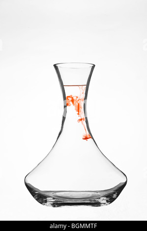 Colorant coloré se dispersant dans l'eau à l'intérieur d'une carafe en verre transparent sur fond blanc. Banque D'Images
