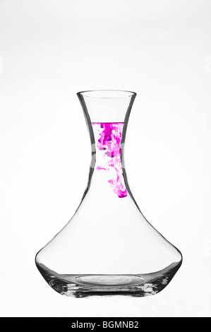 Colorant coloré se dispersant dans l'eau à l'intérieur d'une carafe en verre transparent sur fond blanc. Banque D'Images