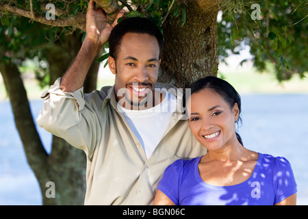 Une happy African American man and woman couple debout à l'extérieur sous un arbre. Banque D'Images