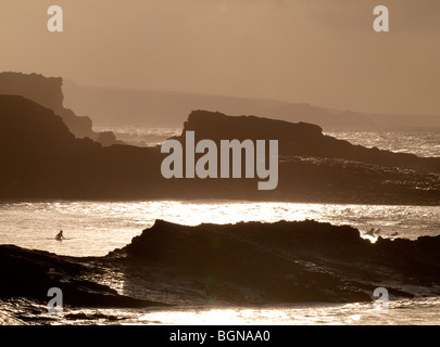Surfer au coucher du soleil entre les rochers, Bude, Cornwall. Banque D'Images