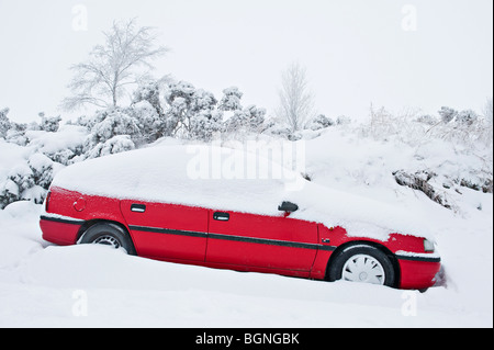 Une voiture rouge coincée dans la neige et abandonnée sur une route de campagne près de Knighton, Powys, pays de Galles, Royaume-Uni Banque D'Images