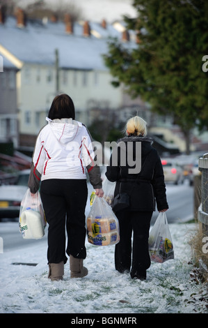 Deux femmes à la maison avec des sacs en plastique plein de shopping de Morrisons, Aberystwyth dans la neige, le 6 janvier 2010 Banque D'Images