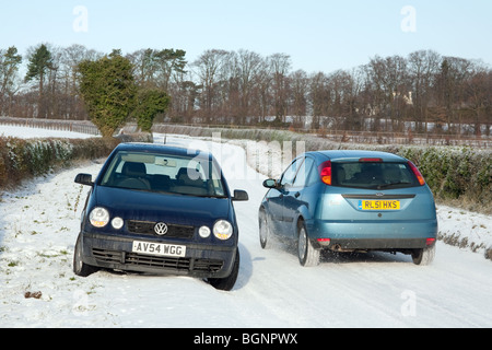 Une voiture conduit passé une voiture garée dans la neige sur une route de campagne, Newmarket Suffolk, UK Banque D'Images