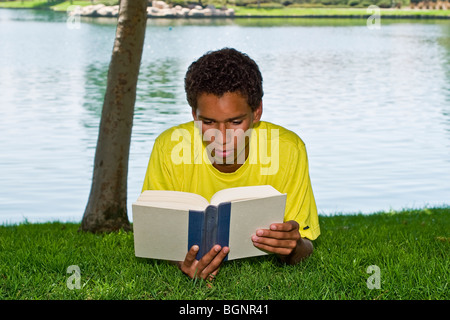 Jeune adolescent de 16 et 17 ans jeune homme se détend dans la lecture de détente sous l'ombre des arbres du parc © Myrleen Pearson Vue avant Banque D'Images