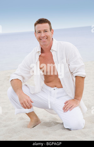 Portrait d'un homme mûr à genoux sur la plage et souriant Banque D'Images