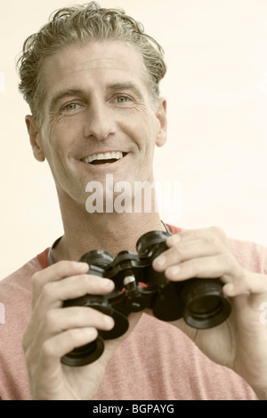 Portrait of a young man holding binoculars and smiling Banque D'Images