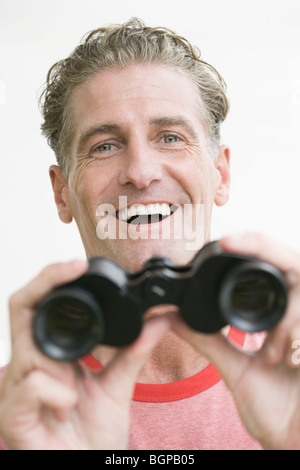 Portrait of a young man holding binoculars et rire Banque D'Images