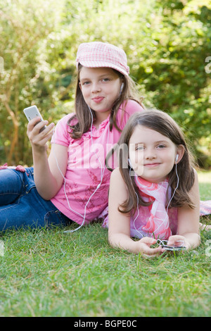 Portrait de deux sœurs à l'écoute de lecteurs MP3 dans un parc Banque D'Images