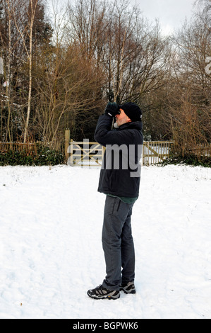 Homme vêtu de vêtements chauds l'observation des oiseaux dans la neige, Gillespie Park la réserve naturelle locale, Highbury London England UK Banque D'Images