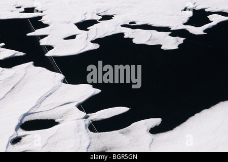 Les modèles de dérive de la neige sur la glace noire sur un lac avec une grande fissure profonde Banque D'Images