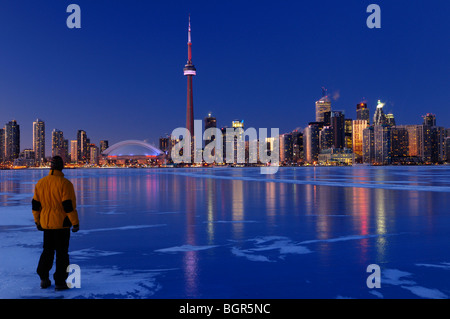 Homme debout sur lac gelé regardant l'Ontario Toronto city skyline lumière jusqu'au crépuscule et réfléchir sur la glace en hiver Banque D'Images