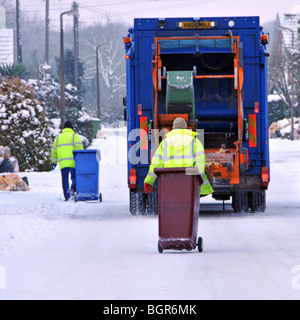 Vue arrière Conseil Dustcart camion binmen au travail portant des vestes d'hiver haute visibilité couvert de neige glacée route résidentielle non traitée Essex Angleterre Banque D'Images