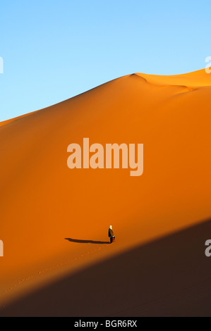 Escalade homme bédouin au coucher du soleil d'atteindre une grande dune de sable dans le désert du Sahara, la Libye Banque D'Images