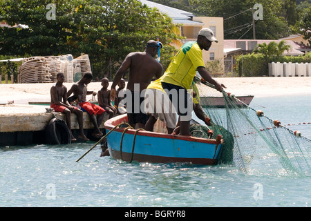 Trois hommes dans un bateau bleu : tirer dans un filet de pêche vu par les garçons sur une jetée, la Grenade, dans les Antilles. Banque D'Images