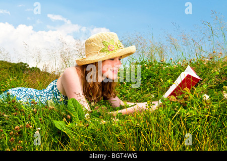 Young Woman Reading book in summer meadow with straw hat Banque D'Images