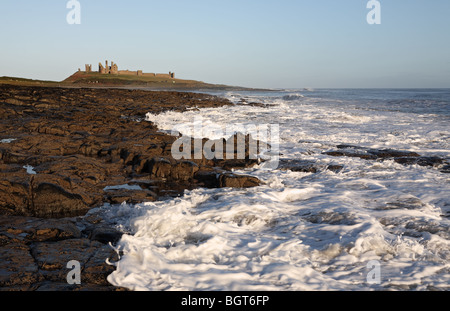 Vagues près de Craster avec Château de Dunstanburgh en arrière-plan, Northumberland, England, UK Banque D'Images