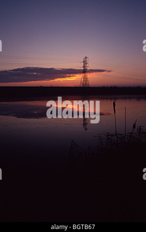 Lea valley Lake avec le soleil se levant au-dessus de lui et d'un pylône d'électricité dans l'arrière-plan Banque D'Images