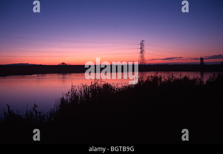 Lea valley Lake avec le soleil se levant au-dessus de lui et d'un pylône d'électricité dans l'arrière-plan Banque D'Images