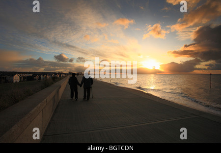 Un couple de personnes âgées marcher main dans la main le long du front de mer à Heacham, Norfolk au coucher du soleil. Banque D'Images