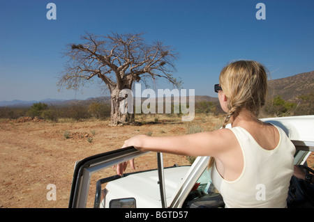 Jeune femme à côté du véhicule à moteur à la recherche au Baobab, Epupa Falls, Kaokoland, Namibie Banque D'Images