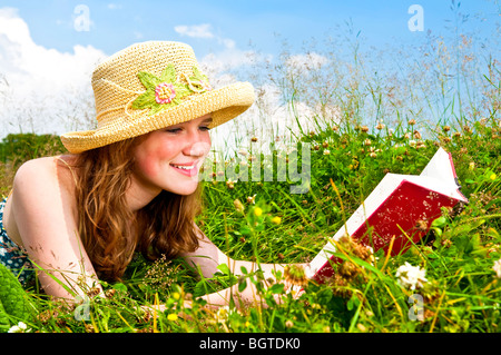 Portrait of teenage girl reading book in summer meadow with straw hat Banque D'Images