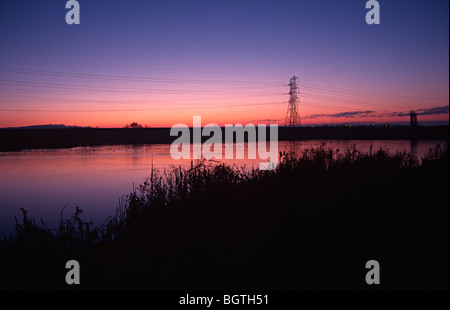 Lea valley Lake avec le soleil se levant au-dessus de lui et d'un pylône d'électricité dans l'arrière-plan Banque D'Images