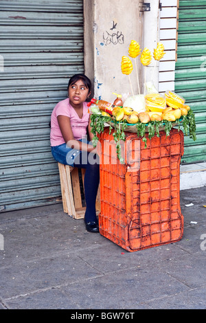 Les Mexicains Indiens tween en minijupe en jean assis sculptés sur les mangues ananas vente trottoir marché Oaxaca Banque D'Images