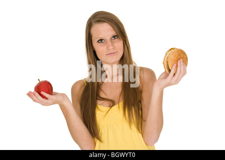 Caucasian woman holding an apple et hambuger essayant de décider lequel de manger Banque D'Images