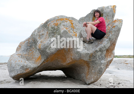 Une femme âgée de 50 ans est assis sur un gros rocher sur la plage de Lesconil près de bénodet en Bretagne Sud, France Banque D'Images