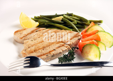 Un repas de steak de thon grillé avec une salade de tomate et concombre et de haricots verts, avec un brin de thym et un quartier de citron Banque D'Images