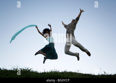 Jeune couple jumping exubérantes avec bras levés portant des expressions de joie Banque D'Images