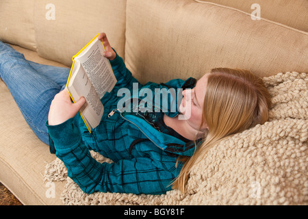 11-13 ans, fille de désinvolture lecture livre sur canapé à la maison. M. © Myrleen Pearson Banque D'Images