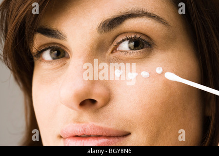 Young woman applying undereye cream Banque D'Images