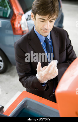 Man taking off gants jetables après l'avitaillement véhicule Banque D'Images