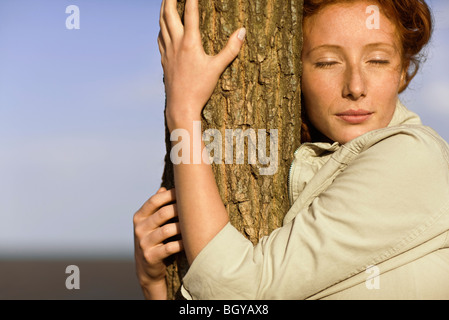 Woman embracing tronc de l'arbre, les yeux fermés Banque D'Images